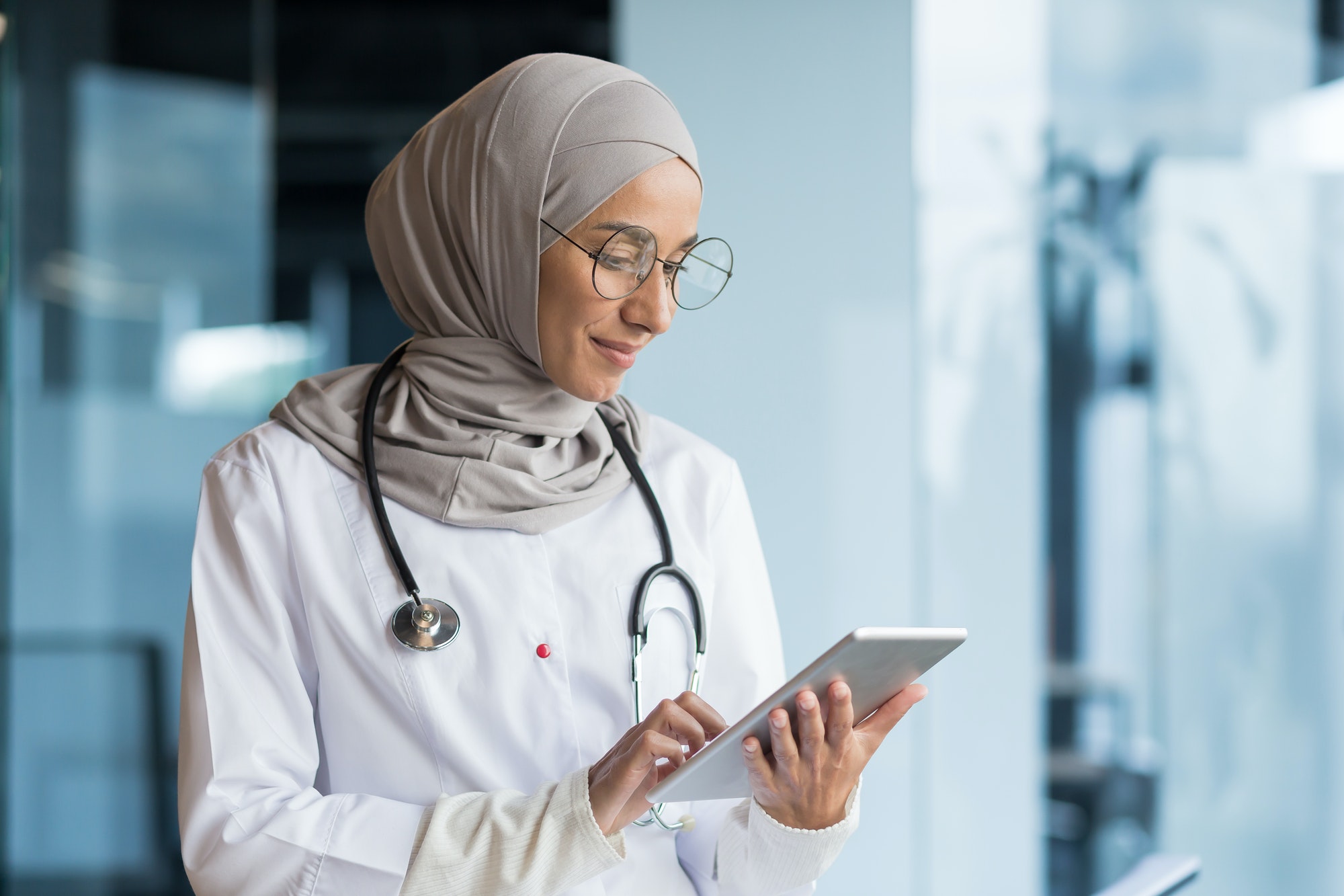 An Arab woman, a Muslim doctor in the hospital. She holds a tablet, concentrates on working, typing