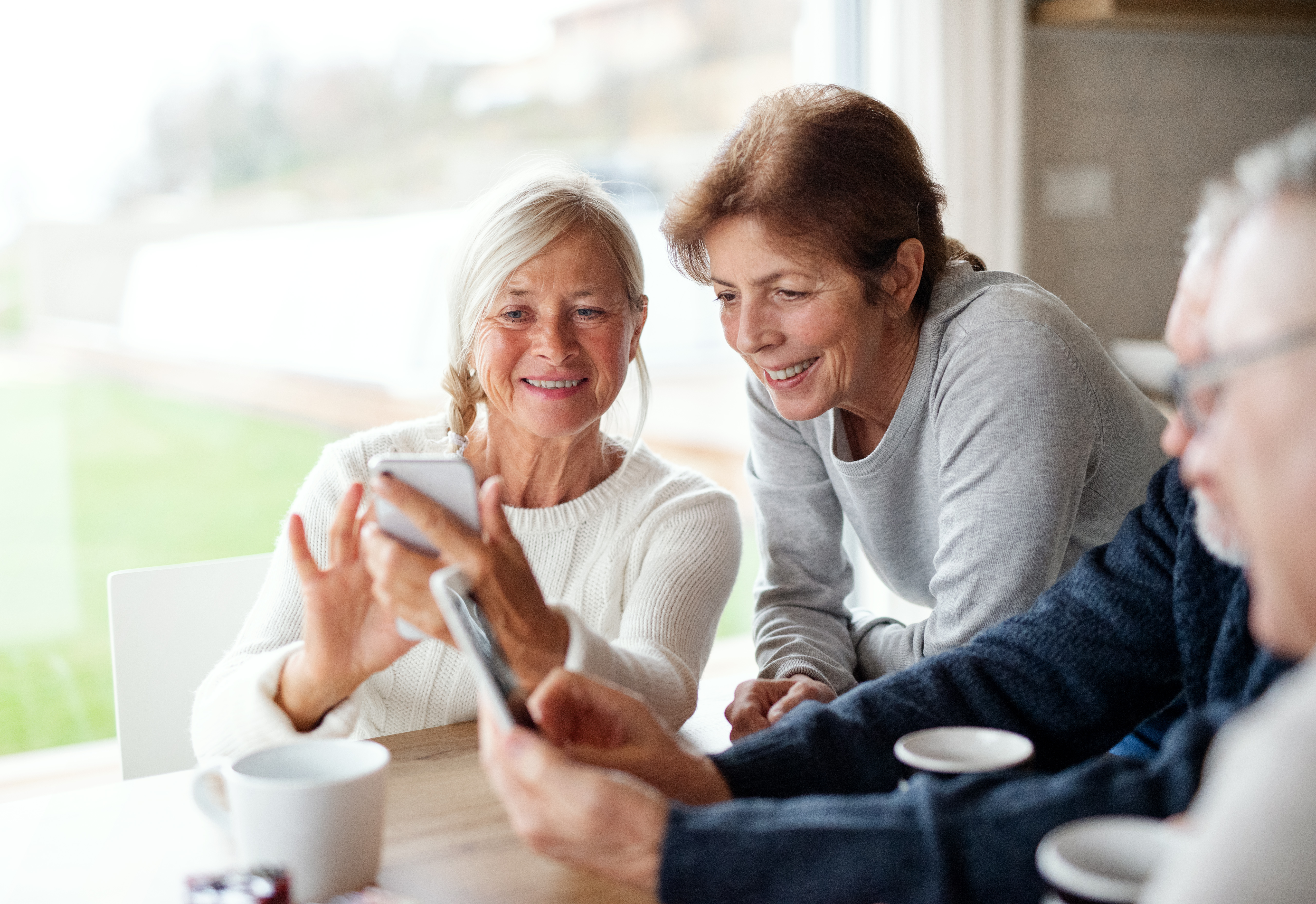 Group of senior friends at home, using smartphones