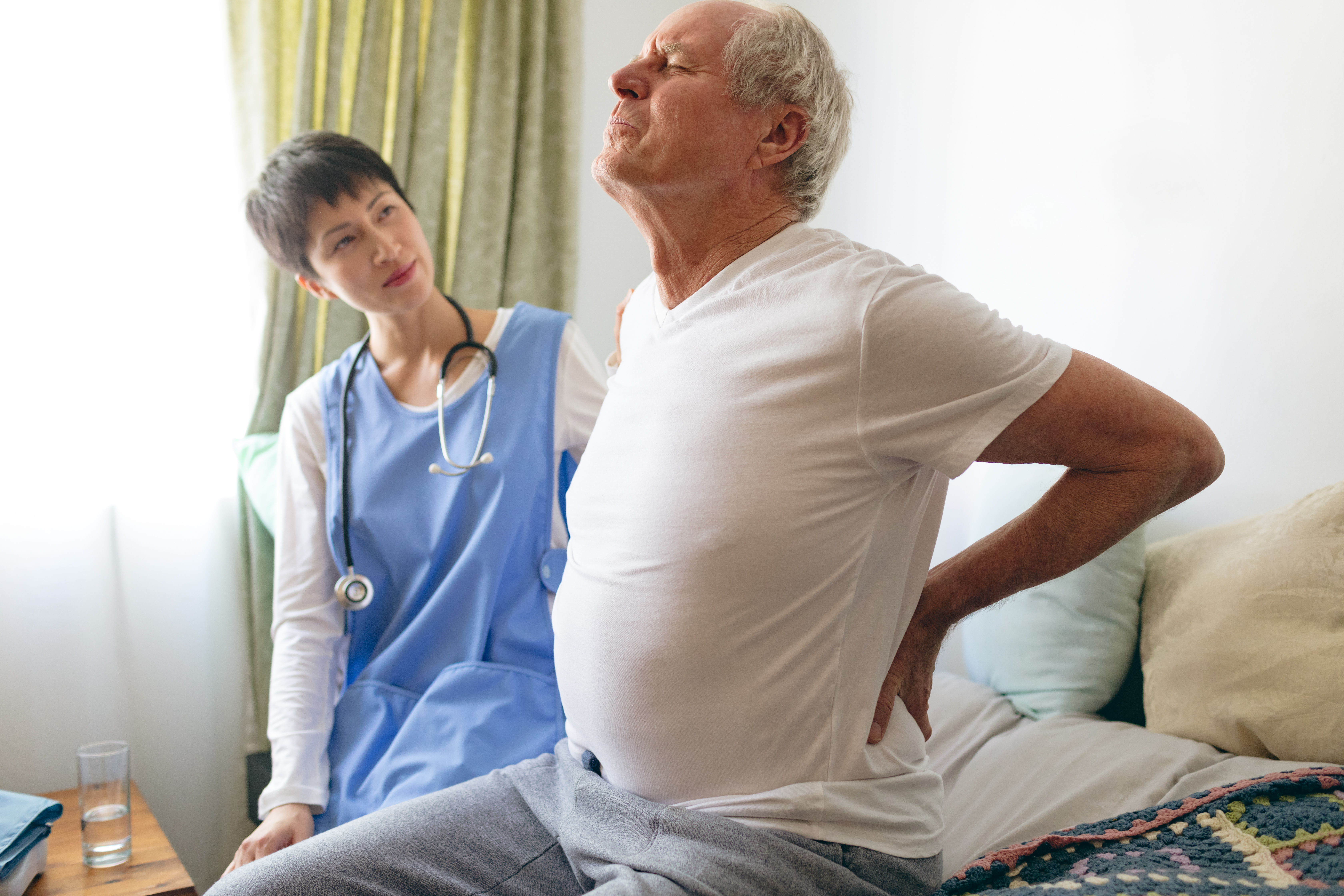 Male nurse helping senior male patient for back pain at retirement home