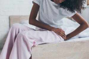 cropped view of african american woman suffering from pain in hip while sitting on bed