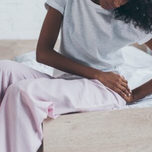 cropped view of african american woman suffering from pain in hip while sitting on bed