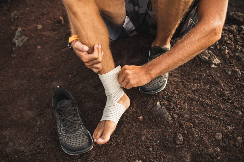 Man bandaging injured ankle. Injury leg while running outdoors. First aid for sprained ligament