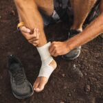 Man bandaging injured ankle. Injury leg while running outdoors. First aid for sprained ligament