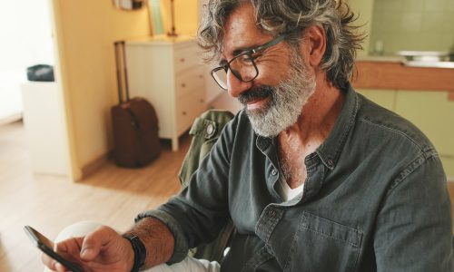 Close-up of an elderly man attentively reading message on his smartphone and drinking coffee